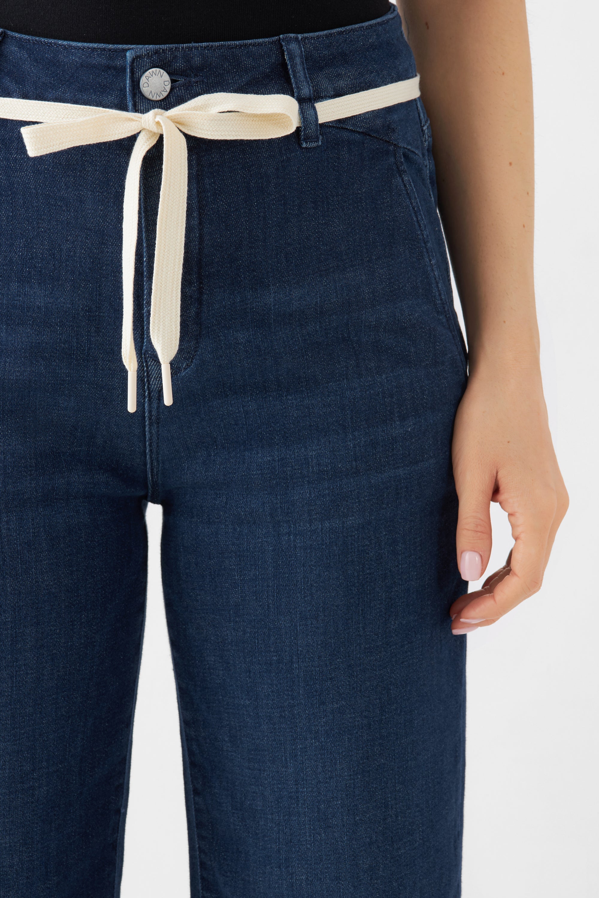 Dunkelblaue DEW Flared-Jeans mit hoher Taille und cremefarbigem Bindegürtel, Nahaufnahme der Vorderseite.