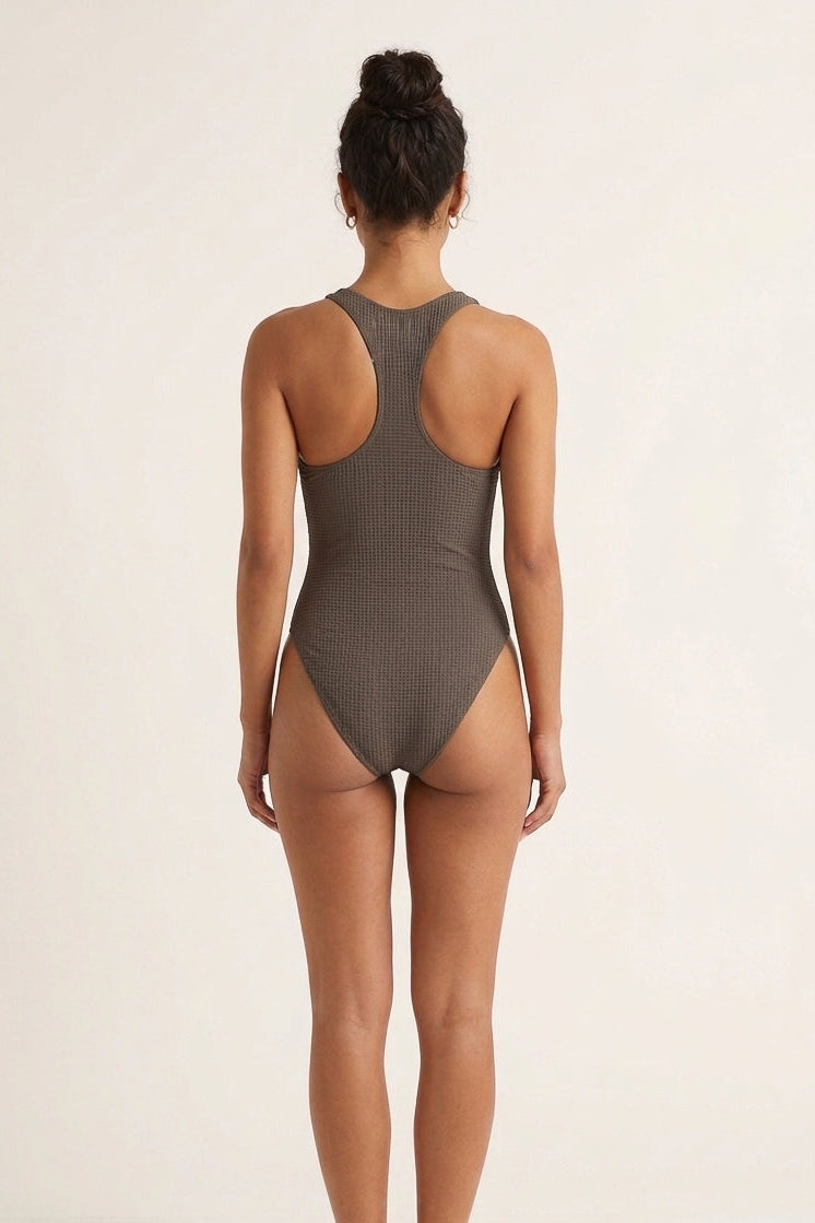 Person wearing a ribbed brown one-piece swimsuit on a beige background