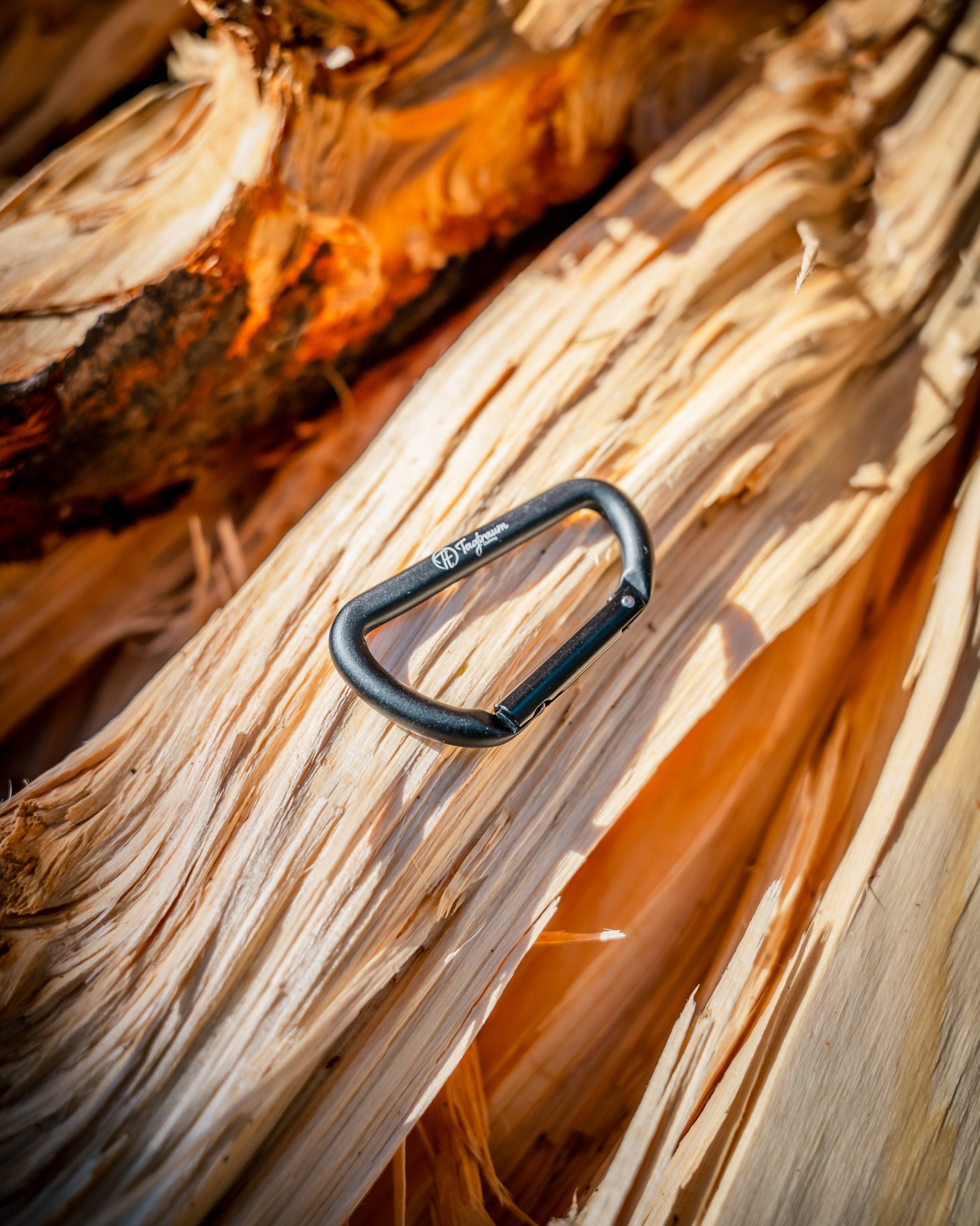 Ein kleiner, schwarzer Karabiner aus 100% Aluminium liegt auf einem Holzstapel