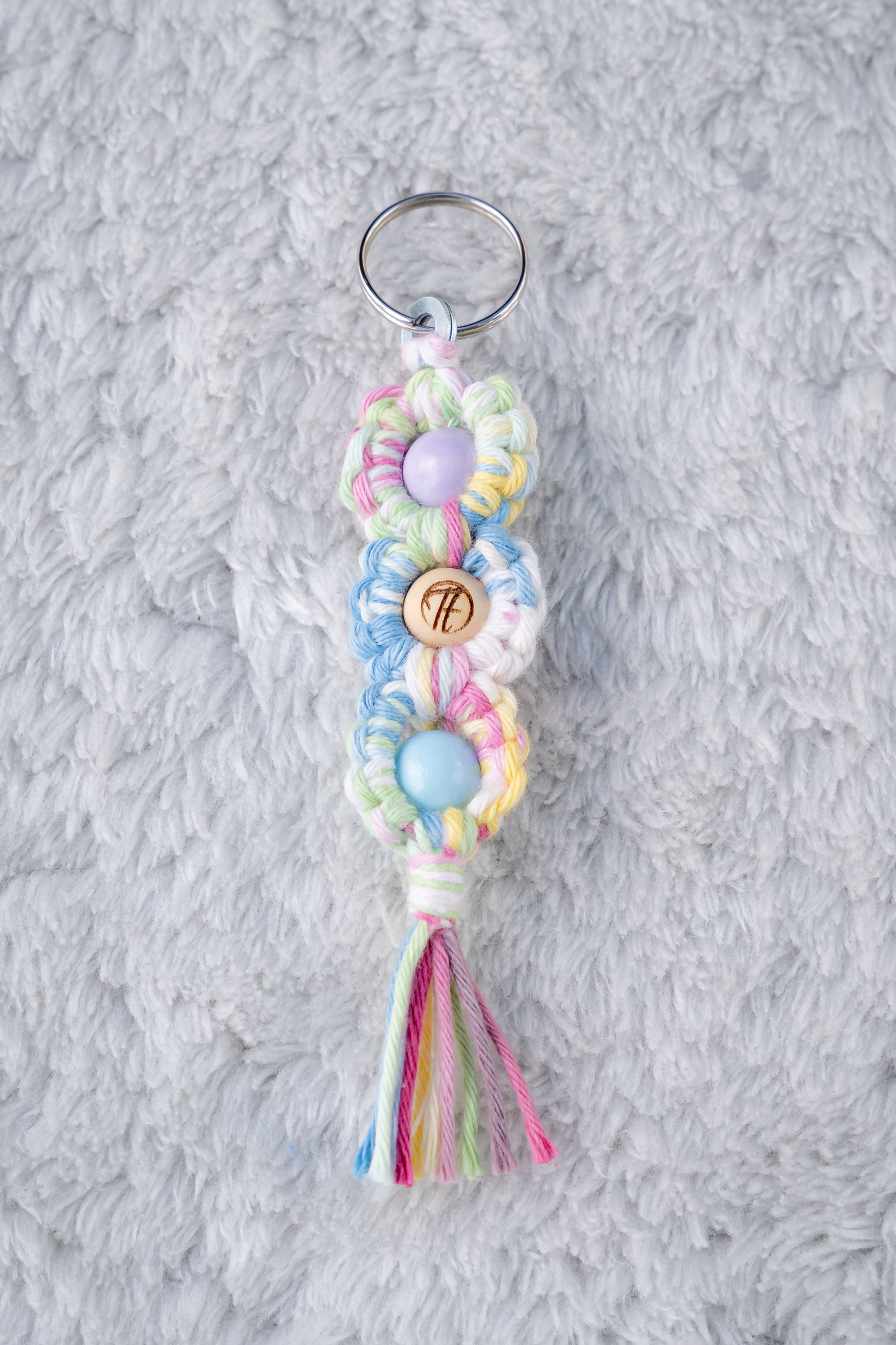 Schöner Makramee Schlüsselanhänger geknüpft aus buntem, farbenfrohem Garn, mit drei Holzperlen, eine davon versehen mit unserem Tagtraum Logo, die anderen Lila und Babyblau. Umweltfreundlich, nachhaltig und handgefertigt von uns in der Schweiz. 