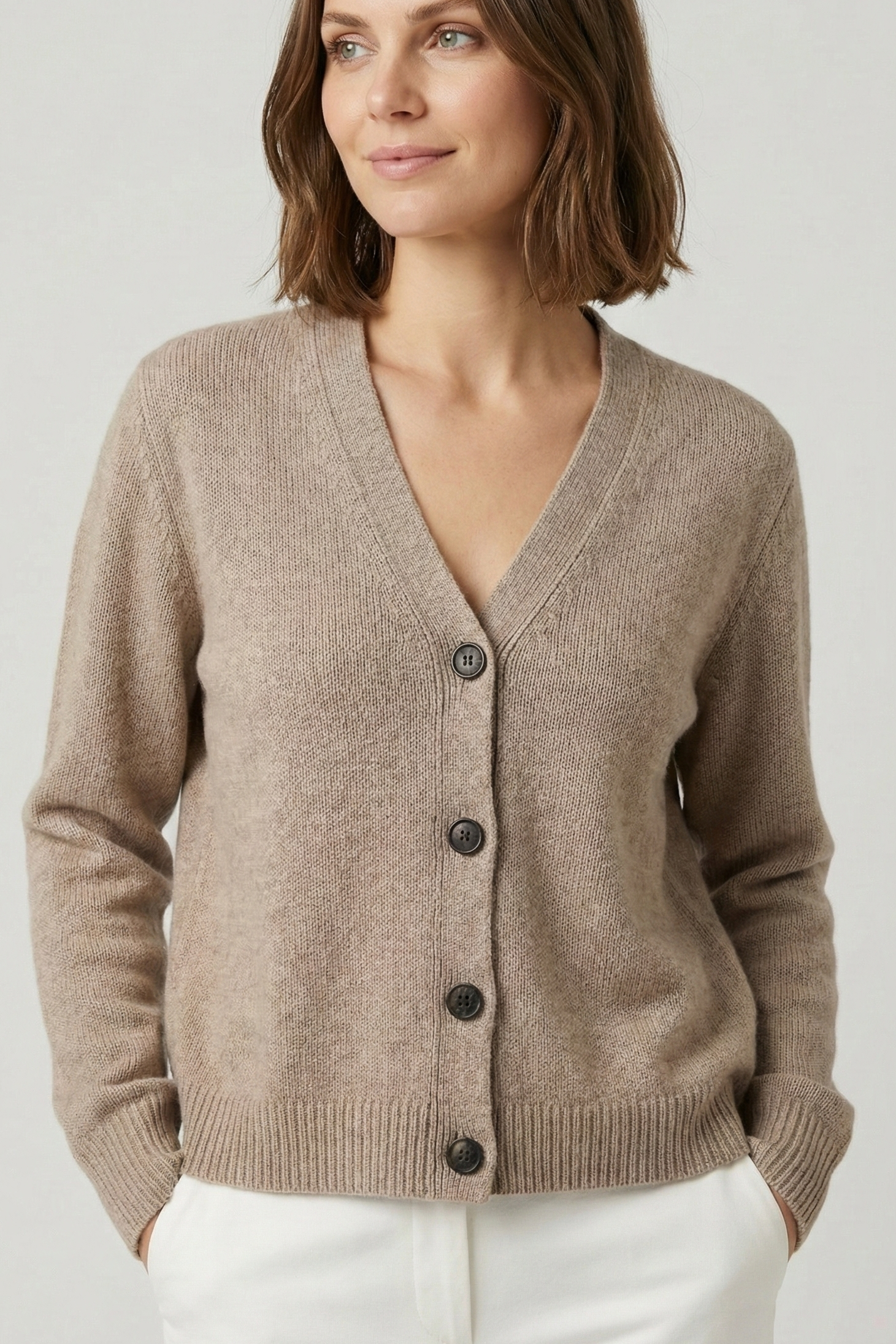 Woman wearing a beige cardigan with black buttons on a plain background