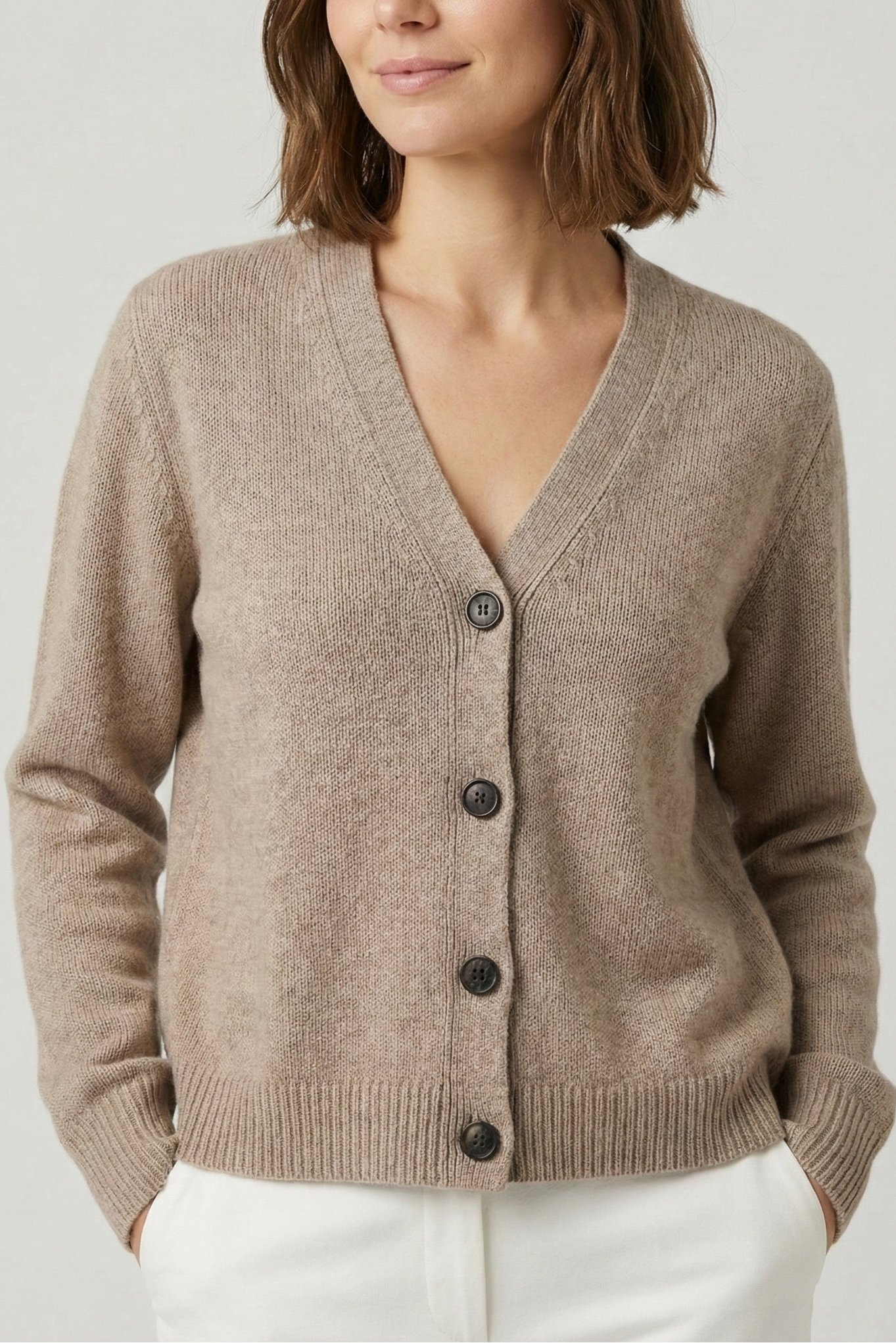 Woman wearing a beige cardigan with black buttons on a plain background